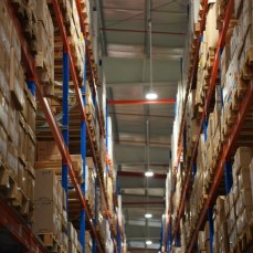 In a factory, photo from the middle of an aisle with stacks of cardboard boxes on either side.